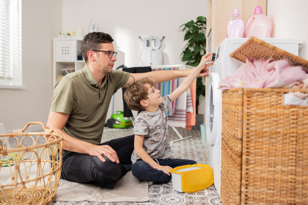 Vater schaltet zusammen mit seinem Sohn die Waschmaschine ein