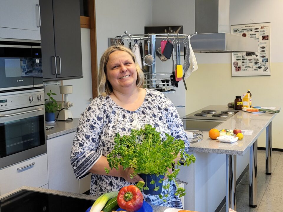 Ernährungsberaterin steht am Herd mit Kräutertopf in den Händen