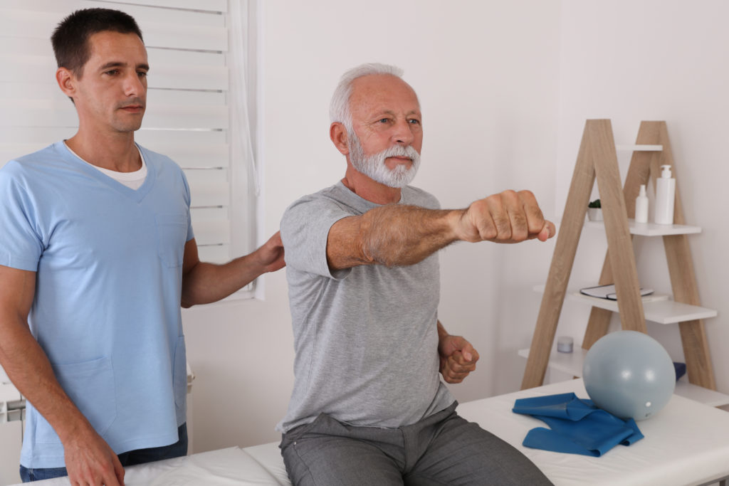 Grauhaariger Mann mit Bart bei der Physiotherapie mit seinem Therapeuten