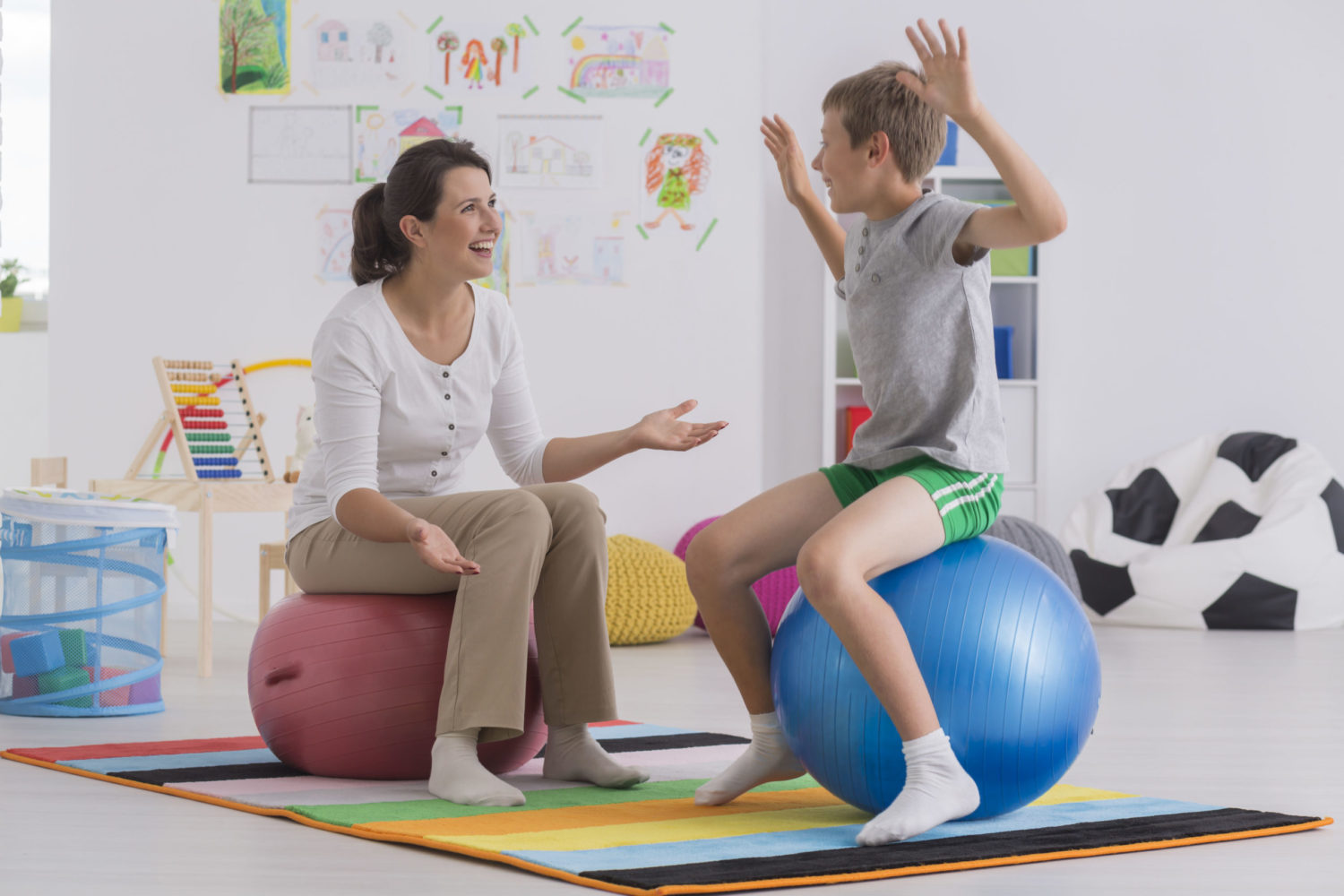 Blonder Junge und dunkelhaarige Frau sitzen auf Gymnastikbällen im Übungsraum